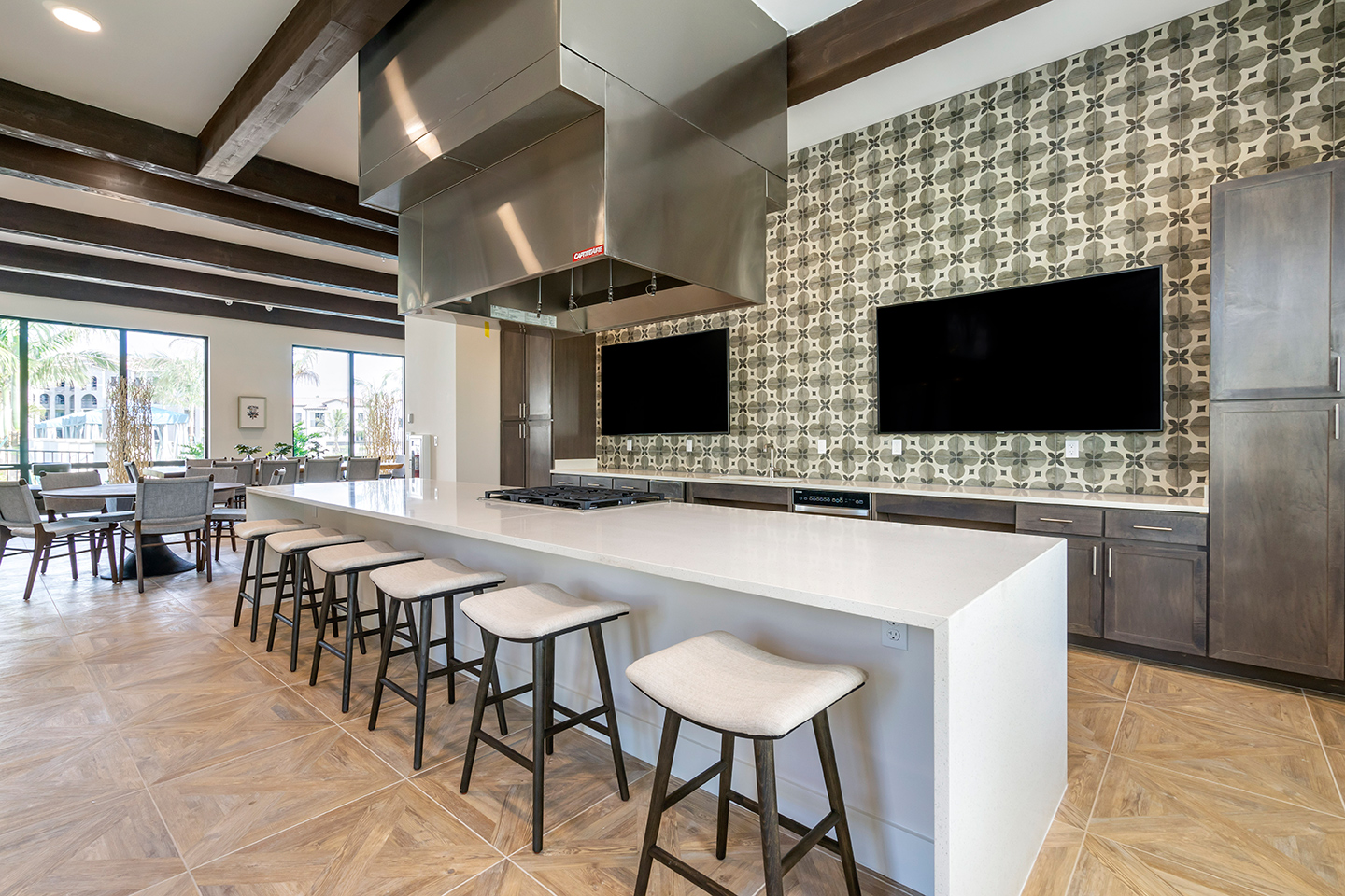 Demonstration kitchen with large TV screens, gas range, cabinets, and barstool seating