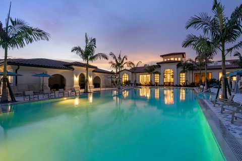 Resort-style pool at dusk with palm trees and lounging areas at dusk