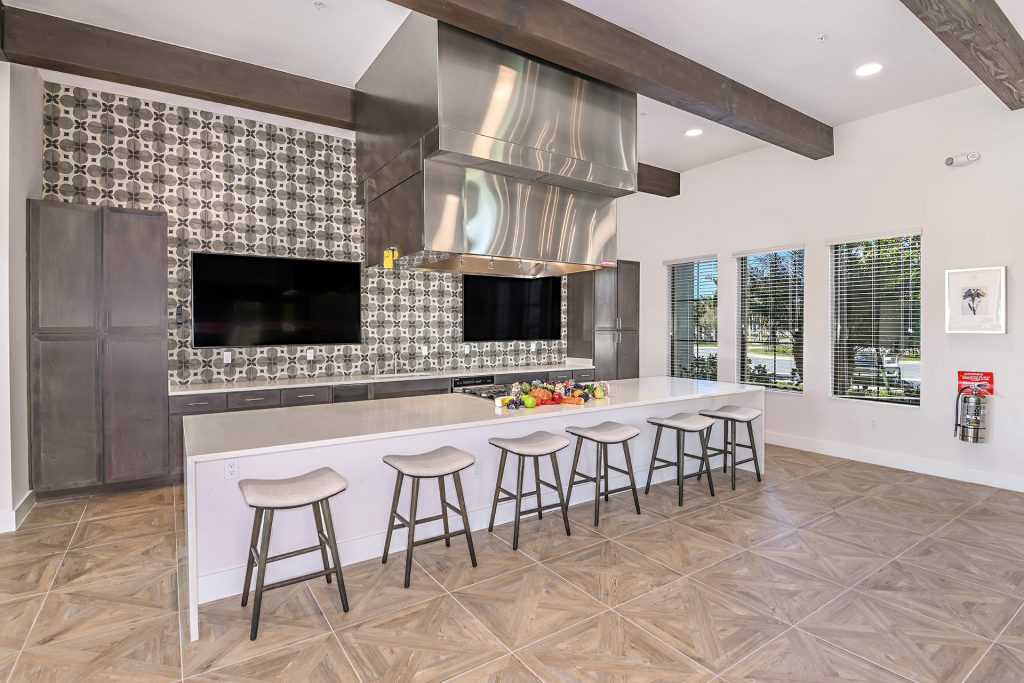 Clubhouse kitchen area with island, single sink, steel appliances, seating, and televisions
