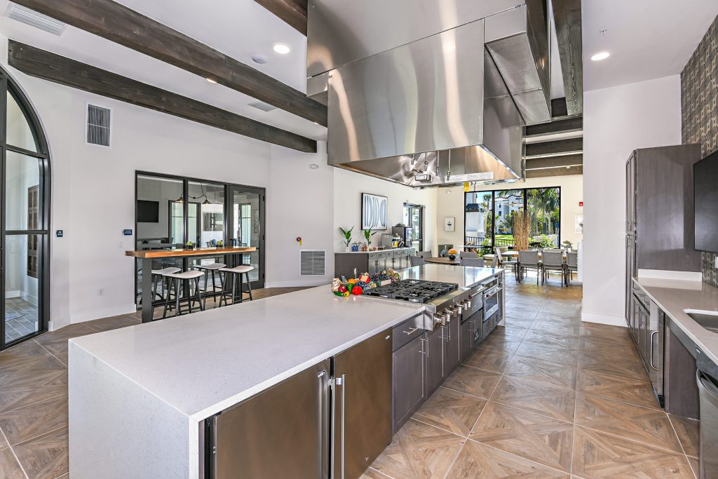 Clubhouse kitchen area with island, single sink, steel appliances, seating, and wall paintings