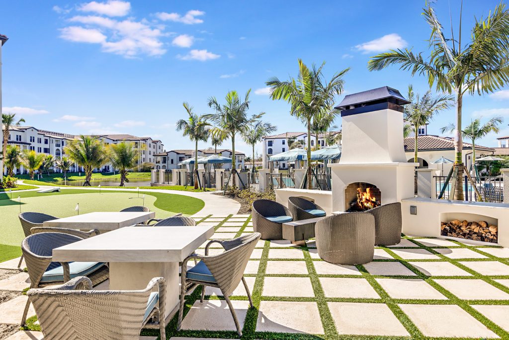 Outside deck with a variety of lounge seating, fire pit, tropical landscaping, and putting green
