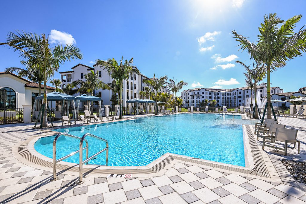 Swimming pool area with shaded seating, tropical landscaping, and water fountain
