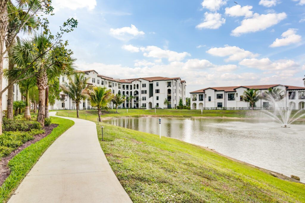 Exterior shot of apartment complex next to pond with fountain surrounded by tropical landscaping