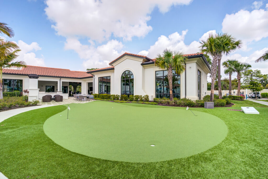 Outdoor putting green and cornhole play area surrounded by tropical landscaping