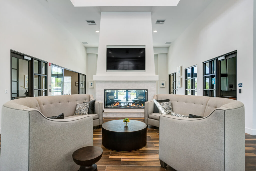 Indoor clubhouse lounge area with couch seating, TV, firepit, and wood-style flooring